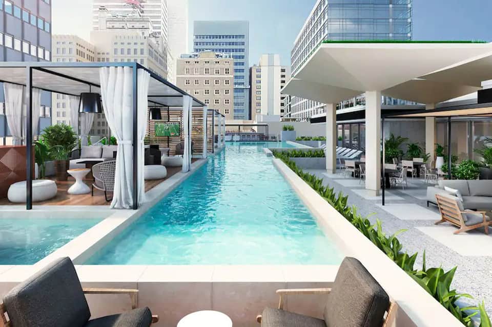 Modern rooftop lap pool with urban skyline, white cabanas, and contemporary architectural design