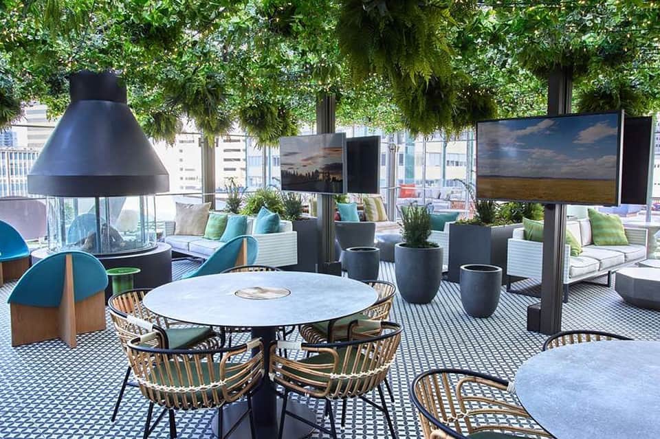 Modern rooftop lounge with round tables, hanging plants, and city skyline views