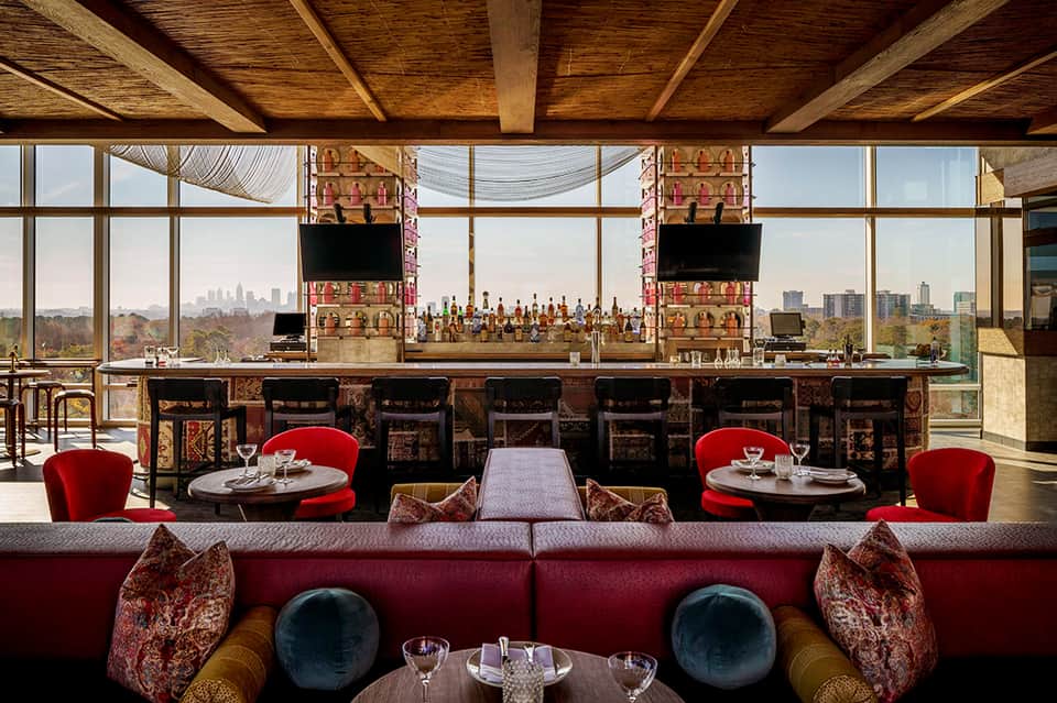 Upscale lounge bar with red seating, wooden beams, and floor-to-ceiling city skyline views