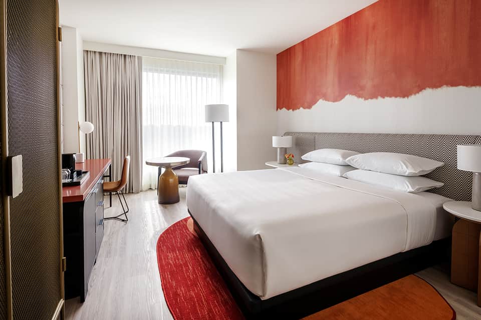 Modern hotel bedroom with red accent wall art, geometric headboard, and ocean-view glass doors
