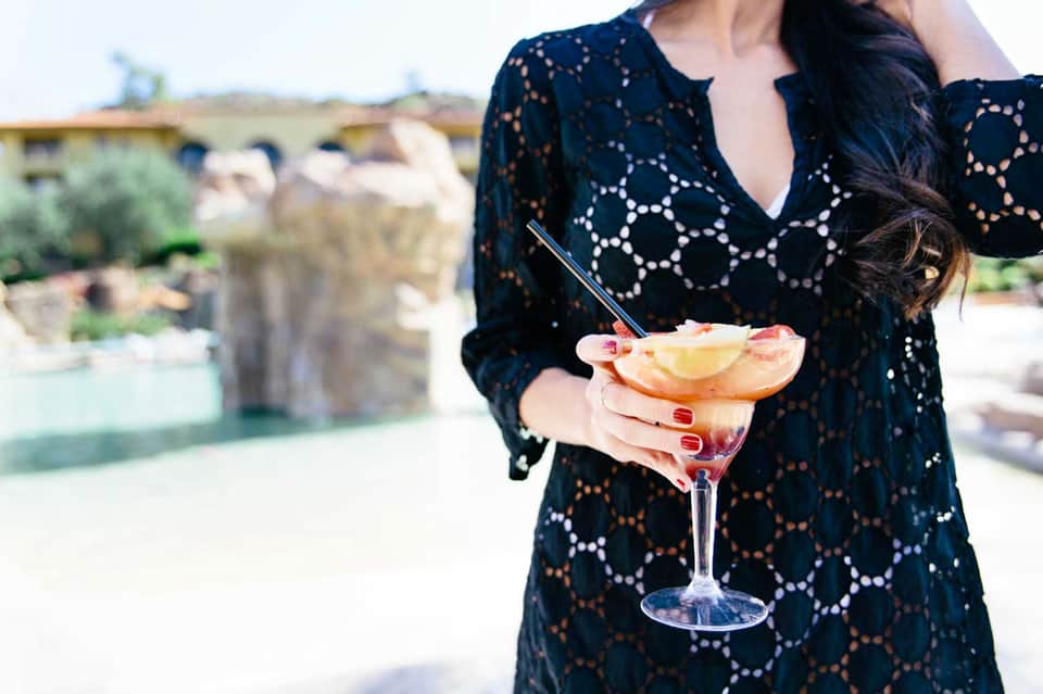 Woman in black lace cover-up holding tropical cocktail with grapefruit garnish at resort