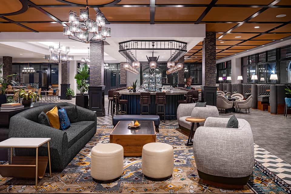 Upscale hotel lobby with bar, chandelier, stone columns, and contemporary furnishings