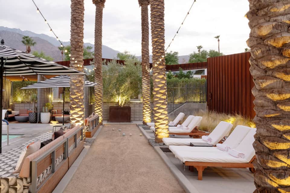 Illuminated palm trees along resort courtyard with lounge chairs and fire feature
