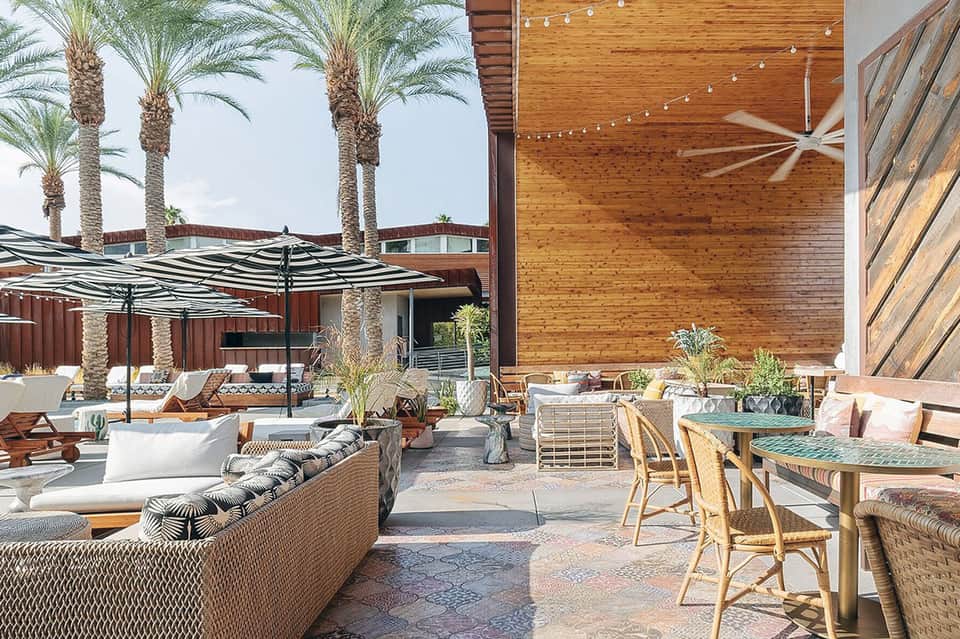 Outdoor terrace with palm trees, striped umbrellas, woven lounge seating, and wooden architectural elements