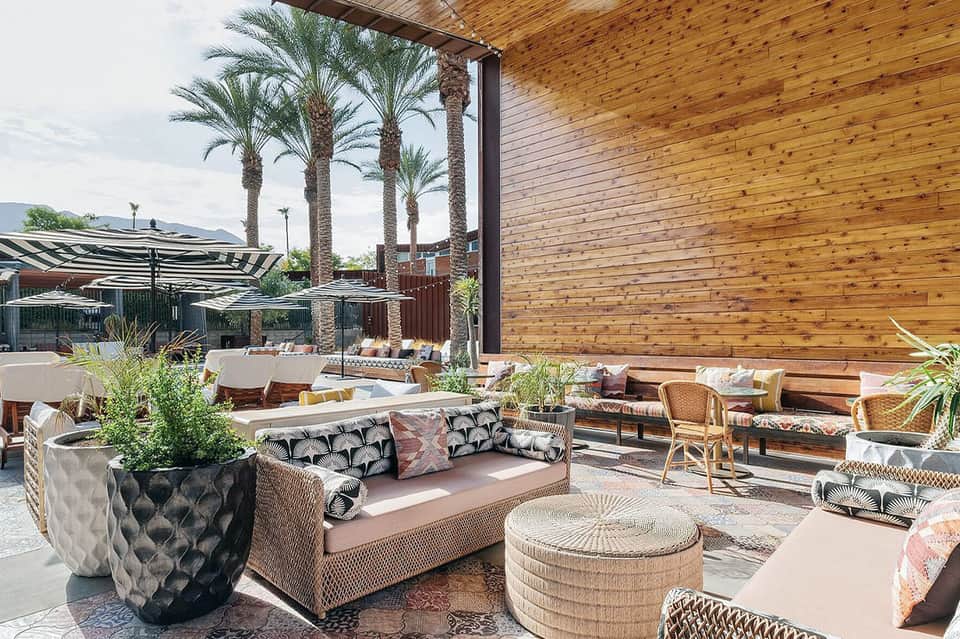 Modern outdoor lounge area with wicker furniture, wooden pergola, palm trees, and fire pit