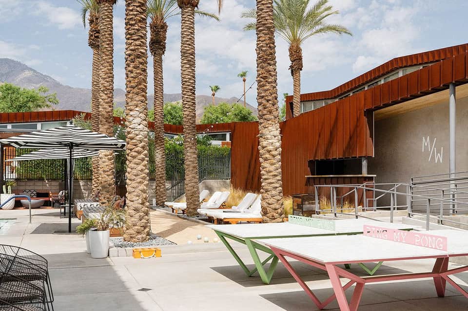 Outdoor lounge area with palm trees, white loungers, and mountain views