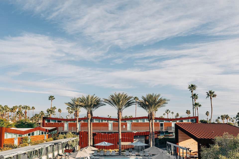 Modern resort pool area with red architectural features and palm trees in desert setting