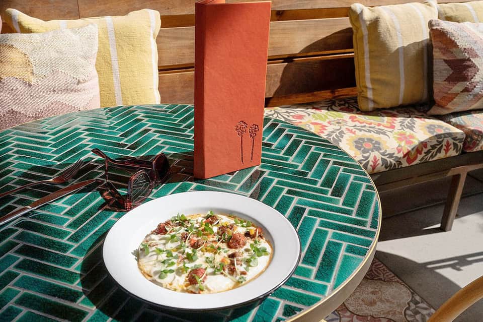 Gourmet flatbread pizza on green patterned table with colorful cushions and pillows