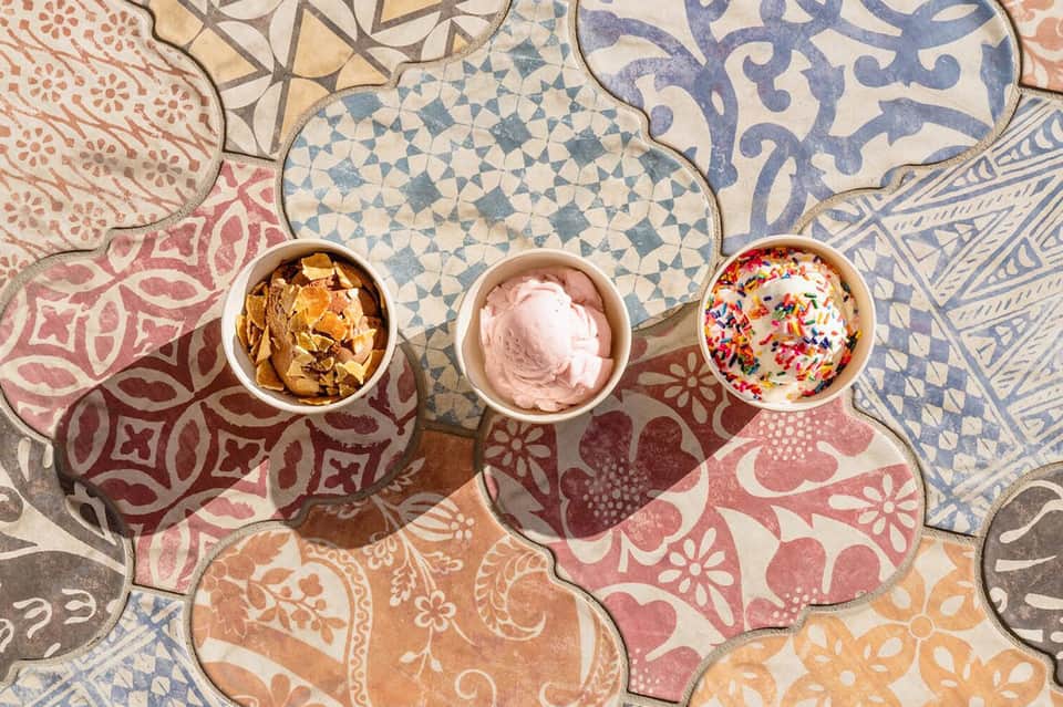 Three ice cream bowls with colorful toppings on decorative Moroccan tile floor