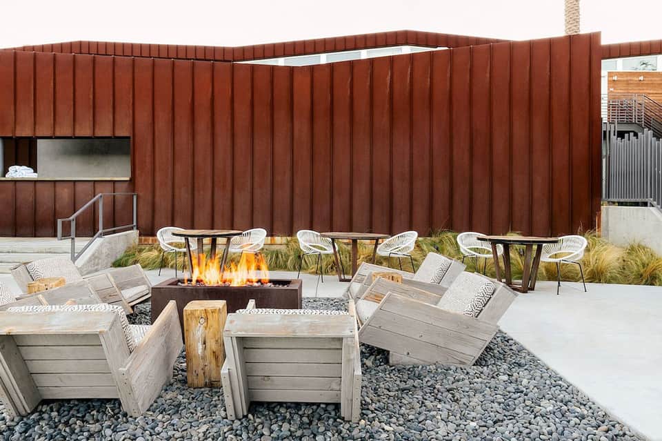 Modern outdoor fire pit area with Adirondack chairs, gravel ground, and contemporary red brick wall
