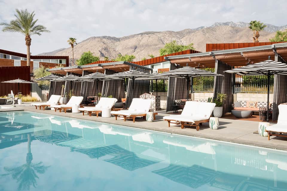 Modern pool resort with striped cabanas, lounge chairs, and mountain desert backdrop