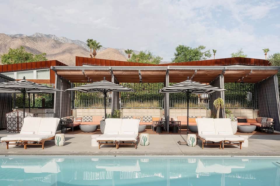 Desert resort pool area with white loungers, striped umbrellas, and mountain backdrop