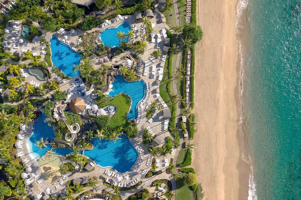 Aerial resort view with multiple blue pools, palm-lined grounds, and pristine white sand beach