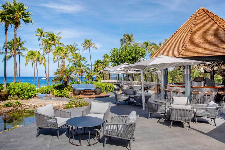 Beachfront lounge with gray furniture, umbrellas, palms, and ocean view