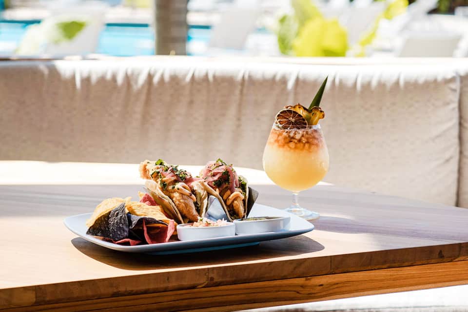 Gourmet appetizers and tropical cocktail on beachside table with pool in background