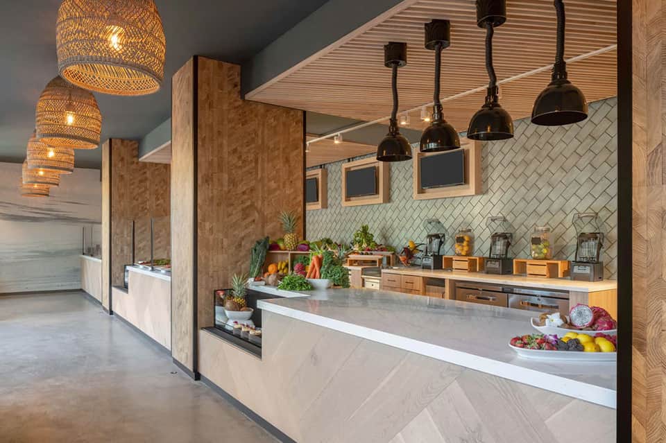 Modern cafe counter with woven pendant lights, white subway tile, and fresh produce display