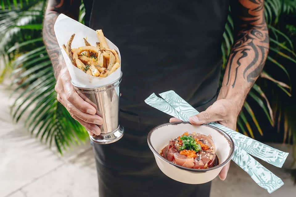 Man holding fried calamari cone and seafood dish near palm trees at resort