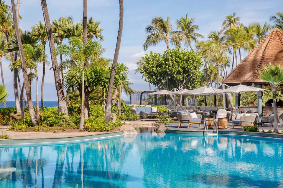 Beachfront resort pool with palm trees, ocean view, and lounge seating