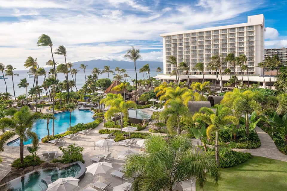 Oceanfront resort with multiple pools, palm trees, and mountains in background