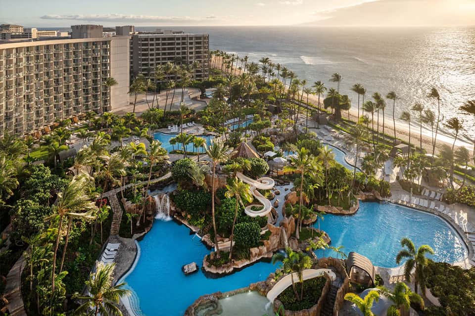 Aerial view of beachfront resort with multiple pools, palm trees, and ocean waves