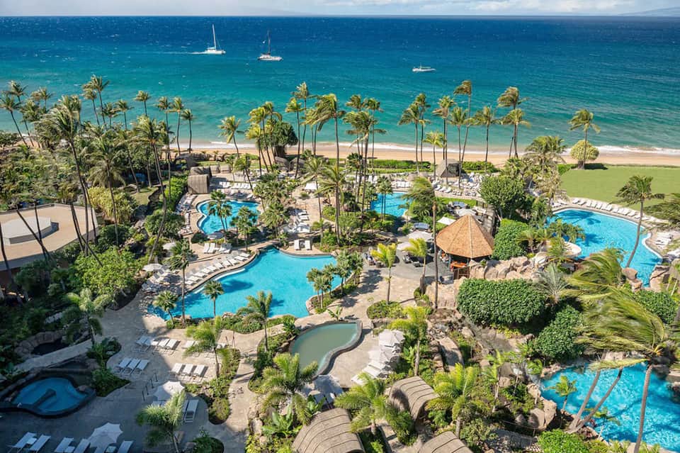 Aerial view of beachfront resort with multiple pools, palm trees, and ocean access