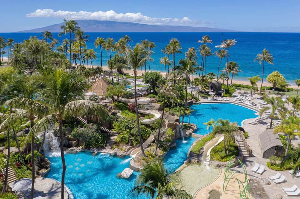 Aerial view of beachfront resort with blue pools, palm trees, and ocean backdrop