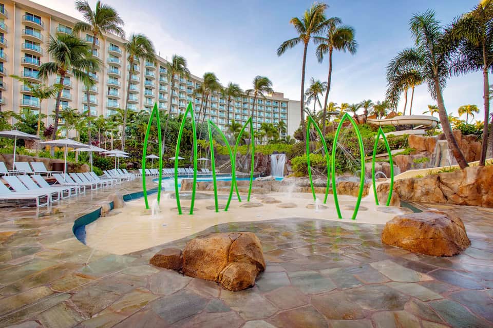 Resort water park splash pad with green arch fountains and sandy pool area