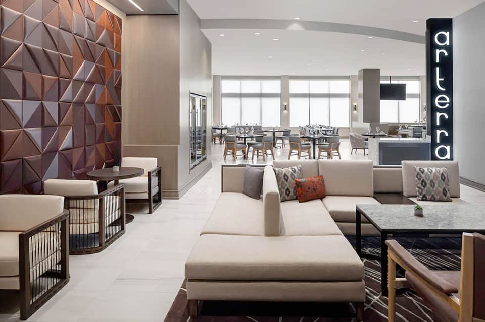 Contemporary hotel lounge with beige seating, textured wall art, and dining