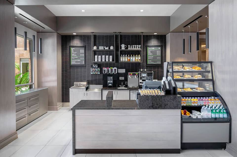 Modern bakery café interior with black tiled walls, espresso machine, pastry display cases, and minimalist contemporary design
