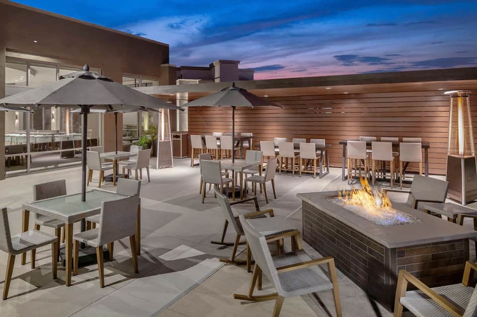 Rooftop terrace at dusk with umbrellas, seating areas, fire pit, and scenic sunset views