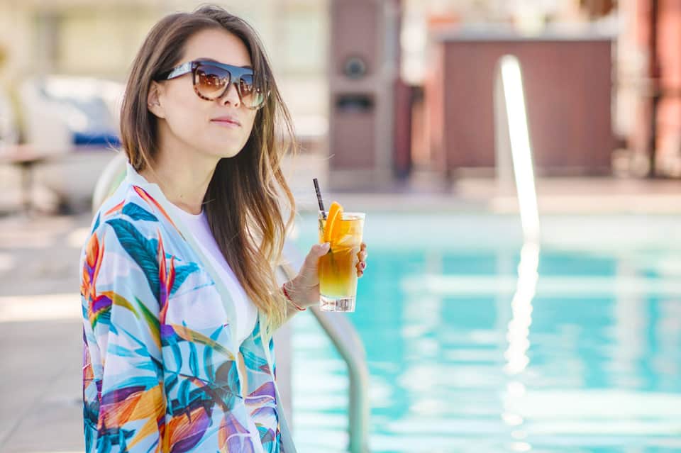 Woman in colorful cover-up holding tropical drink by resort pool