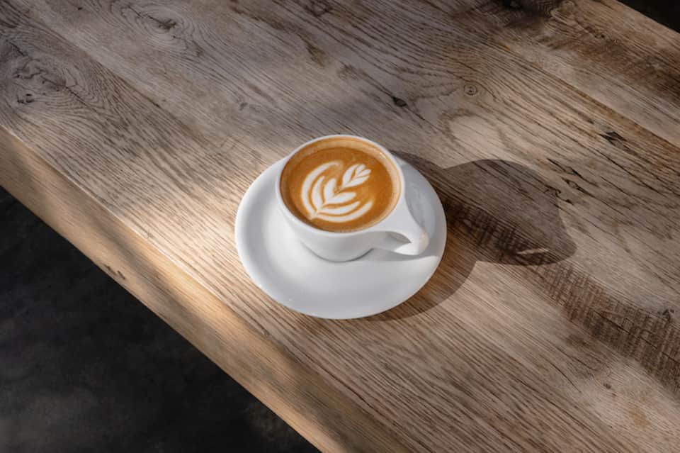 Latte with latte art on white cup and saucer on weathered wood table surface