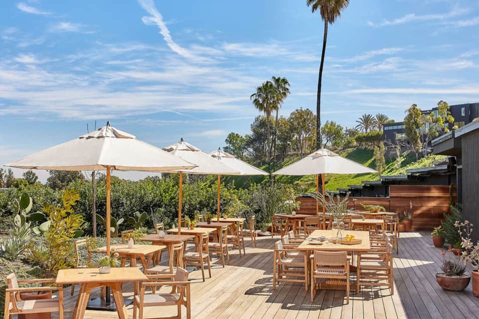 Upscale outdoor terrace with wooden tables, chairs, and large white umbrellas on decking