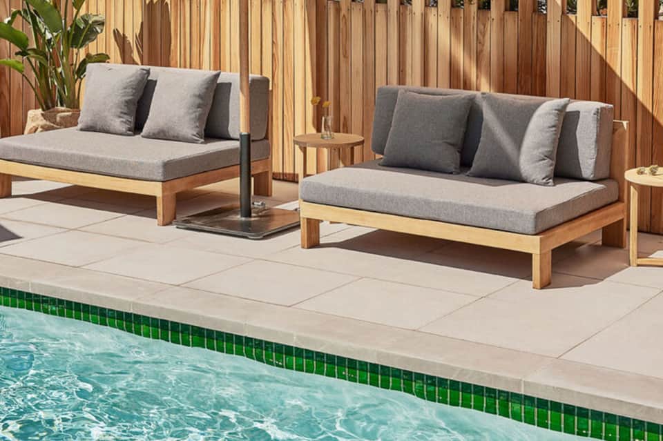 Two wooden loungers with gray cushions beside a turquoise pool and wooden privacy screen