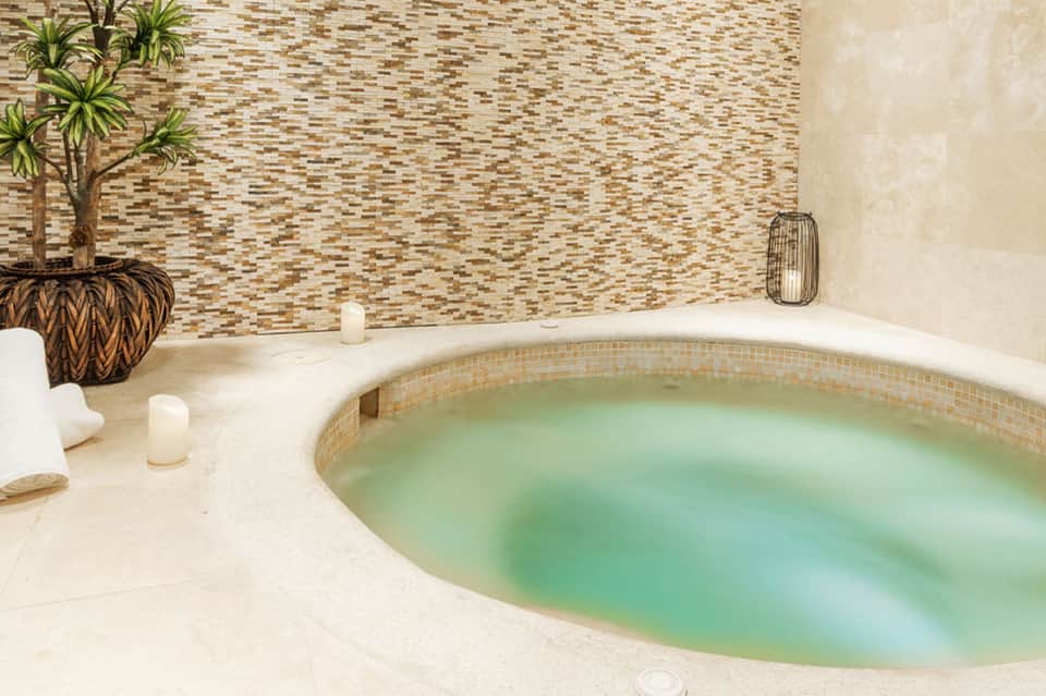 Spa-style hot tub in neutral-toned room with decorative wall tiles and candles