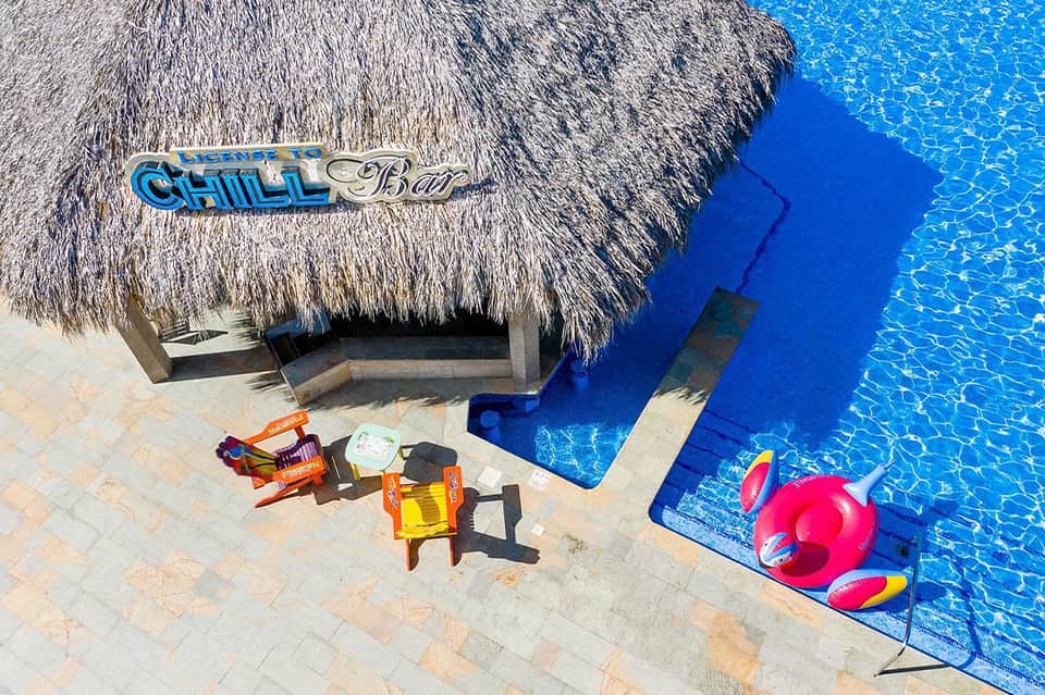 Tiki bar overlooking crystalline blue pool with colorful float toys and palm trees