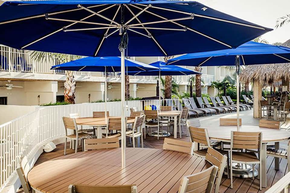 Resort deck with blue umbrellas, wooden furniture, lounge chairs, and palm trees