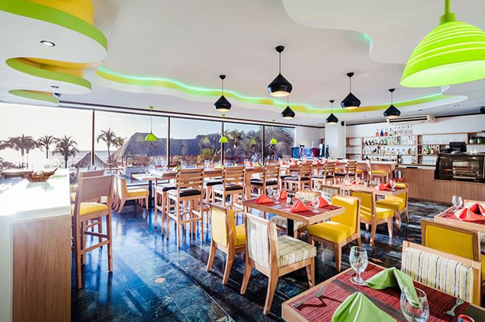 Modern restaurant interior with colorful ceiling design, green lighting, and ocean view windows
