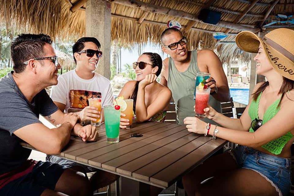 Group of people enjoying tropical drinks at beachside tiki bar under palm thatch