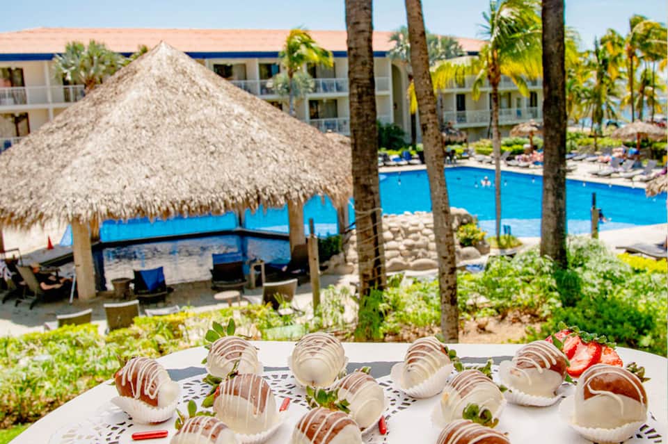 Overhead view of chocolate-covered strawberries and desserts with resort pool and tiki hut in background