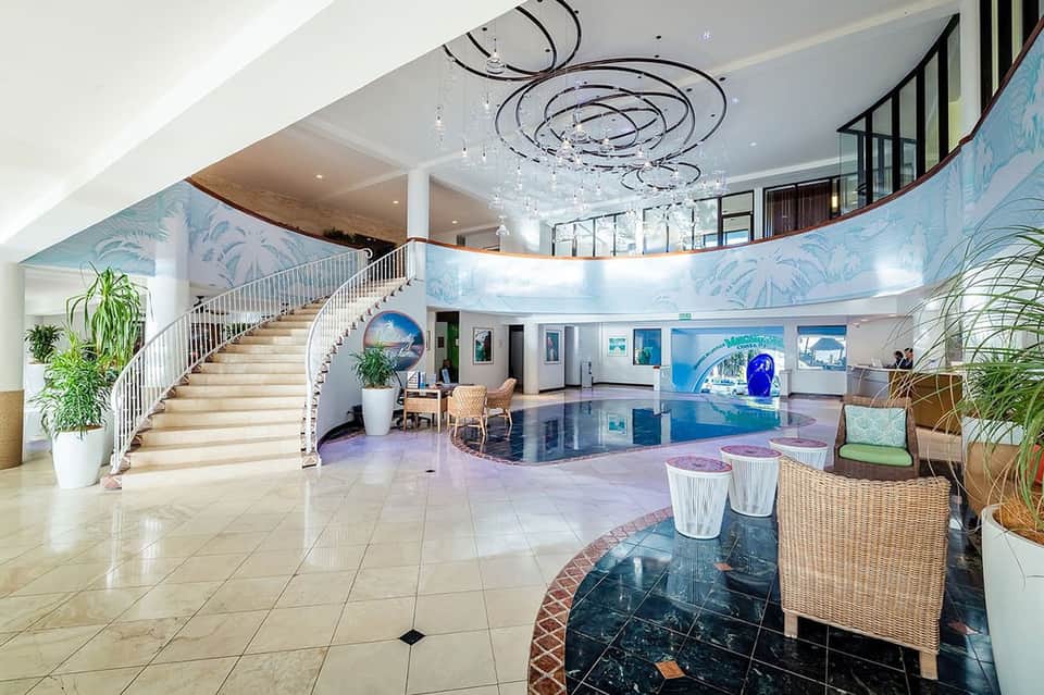 Luxury hotel atrium with curved staircase, modern chandelier, blue tropical murals, and polished marble floors