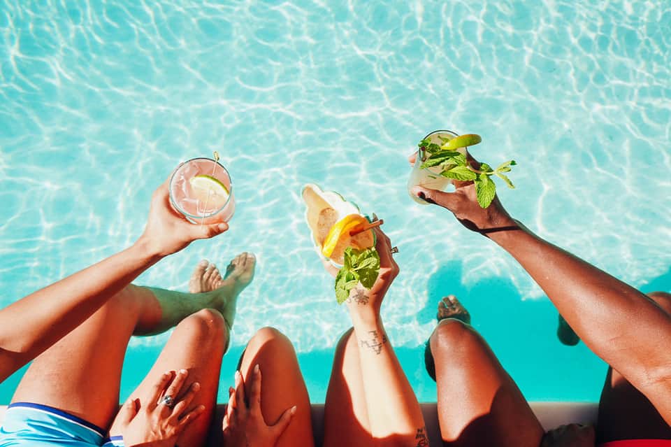 Friends enjoying tropical cocktails and appetizers at poolside with crystal blue water