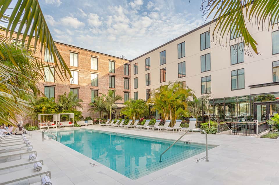 Courtyard pool surrounded by palm trees, white loungers, and brick hotel building