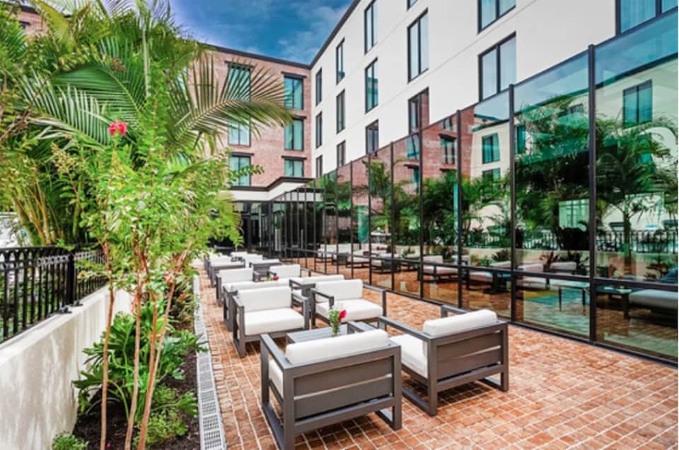 Urban courtyard with lounge seating, tropical plants, glass building facade, and brick paving