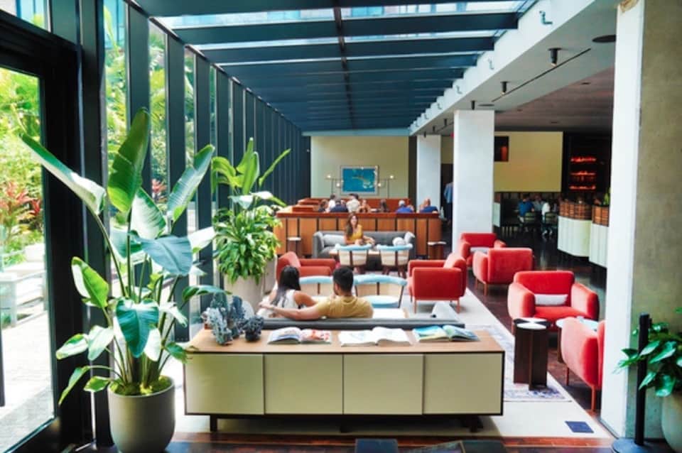 Modern resort lobby with red seating, indoor plants, wooden reception desk, and contemporary multi-level design