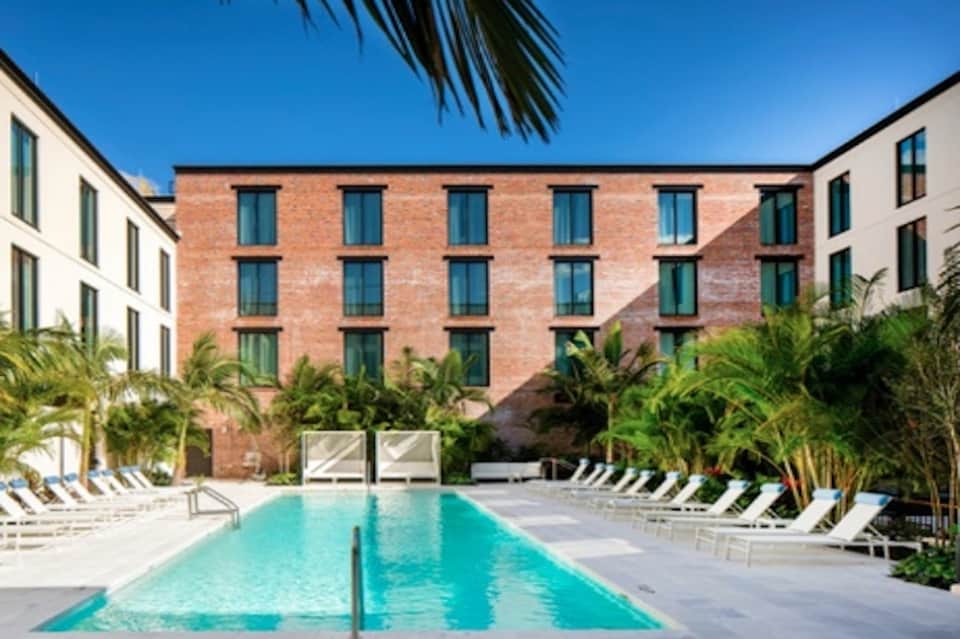 Outdoor courtyard pool surrounded by brick building with palm trees and loungers