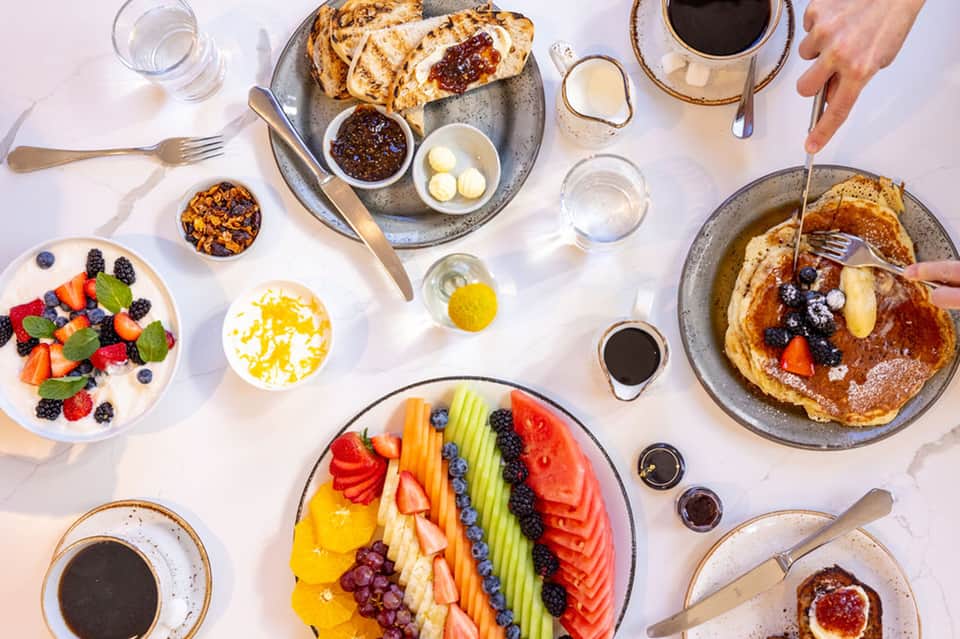 Overhead view of brunch spread with pancakes, fresh fruit platter, coffee, and morning drinks
