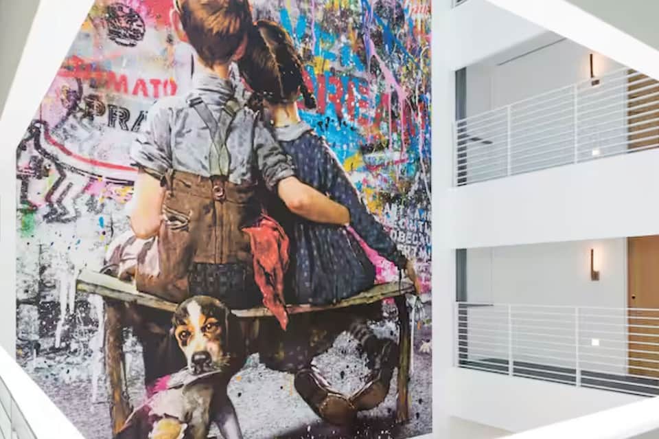Large colorful street art mural of children and dog on white wall indoors