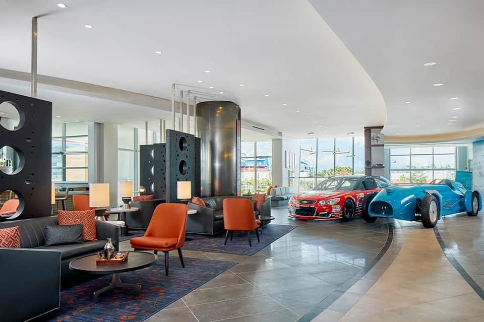 Luxury hotel lobby with modern furniture, sports car displays, and expansive glass windows