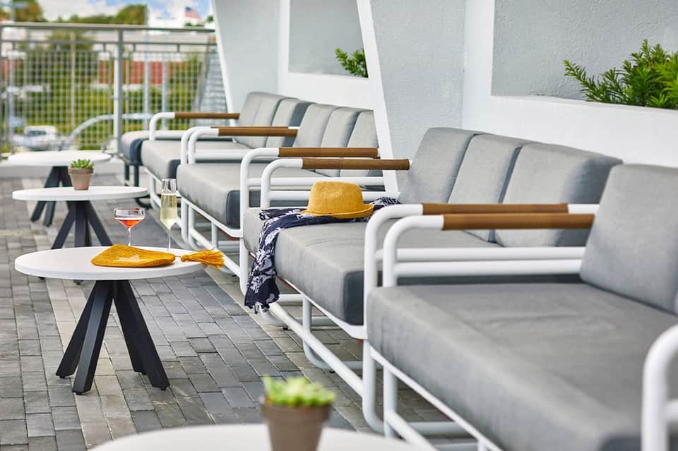 Rooftop lounge with gray cushioned chairs, white frames, and coastal railing